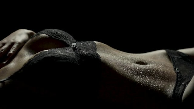 Close-up of a woman's sensual and wet body lying down in black lingerie as she runs her hand down her body