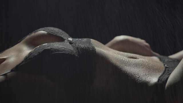 Close-up of a sexy woman's body lying down in black lingerie as rain falls and she runs her hands across her body