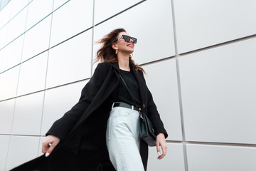 Modern cheerful young hipster woman with a positive smile in sunglasses in black trendy clothes...