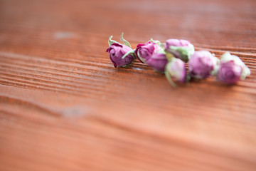 Small dry rosebuds lie on a background of aged wood of red-orange hue