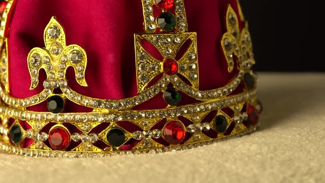 Extreme macro close up of the bottom of ceremonial coronation diamond crown made of gold and red royal soft velvet material. Black background. Slow rotation motion. 4k, uhd.