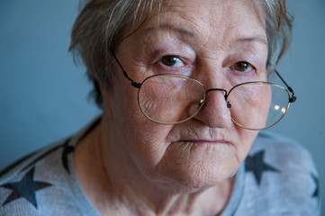 Beautiful elderly woman with gray hair in red glasses with wrinkled face. Retired waiting for guests. Social assistance, care for sick and elderly