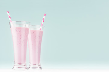 Two blueberry milk cocktails in elegant glass with straws in soft light mint green interior,  copy space.