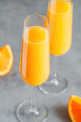 Brunch Mimosa classic cocktail is made from orange juice and sparkling wine or Champagne in flute glasses on a grey table.