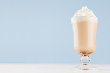 Refreshment coffee drink with whipped cream in transparent wineglass in light blue interior on white wooden table, copy space.