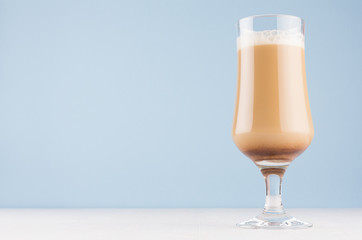 Latte coffee in elegant transparent glass with foam  in modern light pastel blue kitchen interior, copy space.