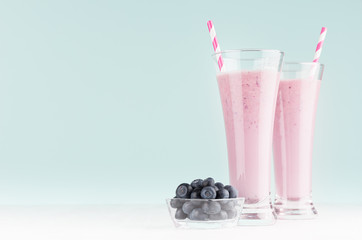 Fototapeta na wymiar Purple milk cocktails with blueberries in bowl, striped straws in elegant glass in soft light mint green interior, copy space.