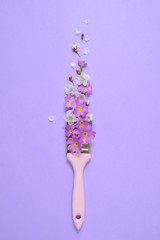 Creative concept. Paintbrush with cherry blossoms and purple flower on pastel purple background. Minimal nature composition with copy space.Flat lay, top view.