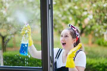 Funny excited woman cleaning windows with spray detergent bottle. Cleaning concept.