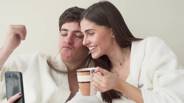 Cute couple is making a selfie on a phone. Man take a strand of his girlfriend's hair and make a mustaches for himself just for fun.