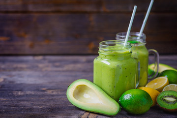 Green smoothie made by avocado, lemon and kiwi on natural wooden background.