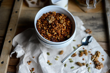 tasty homemade oats granola with nuts and berries in white ceramic bowl served with coconut milk on the wood table for breakfast early in the morning