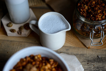 tasty homemade oats granola with nuts and berries in white ceramic bowl served with coconut milk on the wood table for breakfast early in the morning