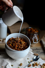 tasty homemade oats granola with nuts and berries in white ceramic bowl served with coconut milk on the wood table for breakfast early in the morning