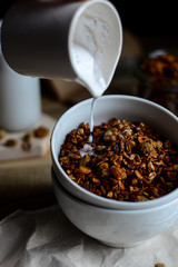 tasty homemade oats granola with nuts and berries in white ceramic bowl served with coconut milk on the wood table for breakfast early in the morning