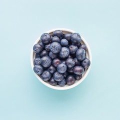 Fresh ripe blueberries in white bowl on a blue bright background