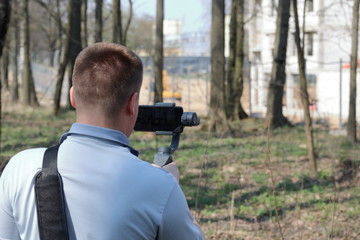 A young man videotaping on a smartphone. Uses gimbal to get smooth footage. Closely watching the movie shooting.