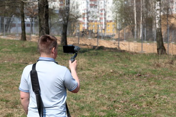 A young man videotaping on a smartphone. Uses gimbal to get smooth footage. Closely watching the movie shooting.