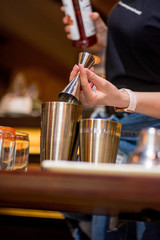 Fototapeta na wymiar Bartender pours liquid into the jigger. Female bartender preparing cocktail in a cocktail bar