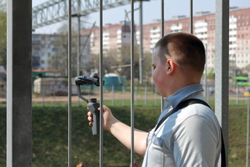 Obraz premium A young man videotaping on a smartphone. Uses gimbal to get smooth footage. Closely watching the movie shooting.