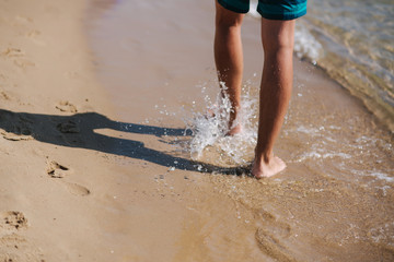 Back view of man bare foot walking on the summer beach. Close up leg of man walking in the sea, splash around