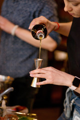 Bartender pours liquid into the jigger. Female bartender preparing cocktail in a cocktail bar