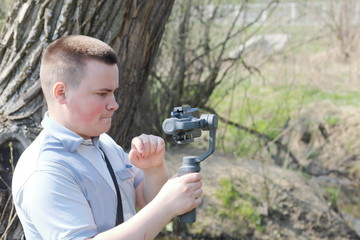 A young man videotaping on a smartphone. Uses gimbal to get smooth footage. Closely watching the movie shooting.