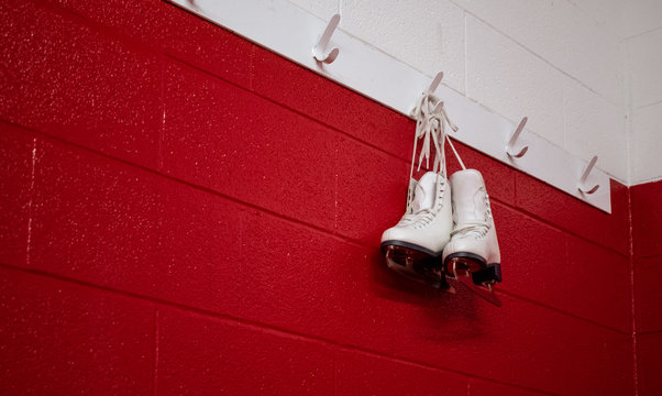 Figure skates hanging over red wall in locker room with copy space