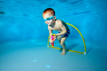 Cute baby dives underwater and pulls toys from the bottom of the pool. Portrait. Underwater...