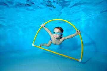 A little boy is engaged in swimming underwater in the pool near the bottom, posing with a yellow...