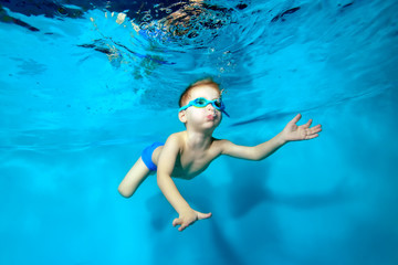 Happy little boy swimming underwater in the pool and blowing bubbles on blue background. Portrait. Underwater photography. Horizontal orientation