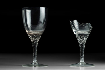Two crystal wine glass on a black mirror background. New and broken.