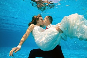 Happy bride and groom kissing underwater in the pool on a Sunny day. The groom hugs and holds the bride in his arms at the bottom. Portrait. Concept. Wedding underwater. Horizontal view