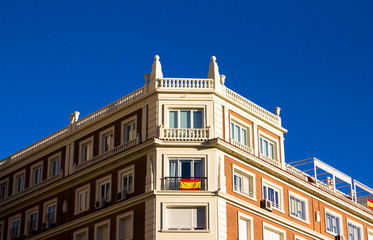 Fototapeta na wymiar Spanish residential building facade with Spanish flag in the window and blue cloudless sky above in Madrid, Spain. Architecture. Sunny day.
