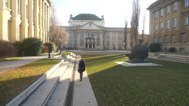 Young woman walking away from camera trough the park in front of the Croatian State Archives