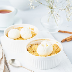 Close up apple crumble with ice cream, spoon with streusel. Side view, vertical. Morning breakfast on a light gray table.