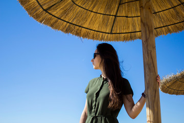 Beautiful attractive girl in sunglasses and in a green dress is standing on a sunny day under a...