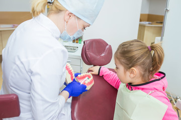 Little girl sits in a dental chair as a patient and doctor explain how to brush teeth. Kid health care, dentistry, medicine concept. Doctor and patient