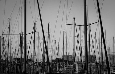 Yacht masts and various yachts on the foreground and city center on the background in Marseille bay. Evening time. Provence, France. Black and white photo. Marine view.