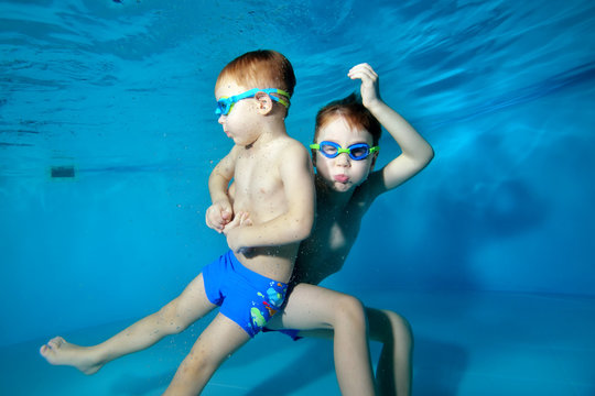 Two children swim and have fun under the water in the pool near the bottom on a blue background. Portrait. Underwater photography. Horizontal orientation of the image