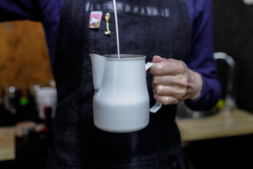 Young barista girl pouring milk in pinscher.