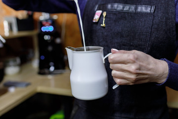 Young barista girl pouring milk in pinscher.