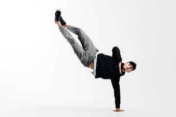 Stylish young man is dancing breakdance. He is standing on one arm and lifting both legs up. - obrazy, fototapety, plakaty