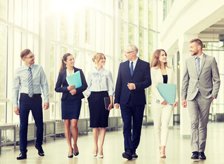 Fototapeta premium people, work and corporate concept - business team with folders walking along office building and talking