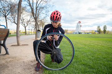 Young cool male cyclist in sportswear and protective helmet repairing air chamber of bike wheel in...