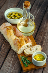 Sliced freshly baked ciabatta bread on wooden cutting board on rustic table with rosemary, salt, olives, and olive oil. Italian food concept.