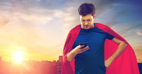 super power, technology and people concept - young man in red superhero cape using smartphone over...