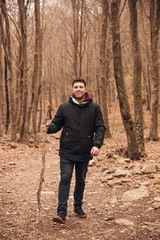 Boy with a beard walking through forest in autumn with a stick