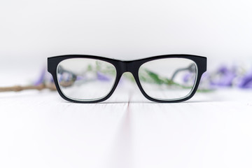 lentes de pasta negros sobre fondo blanco y flores purpuras