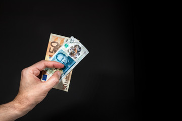 A male hand holding a five pound and 50 (fifty) Euros banknotes, brexit concept, isolated over black.